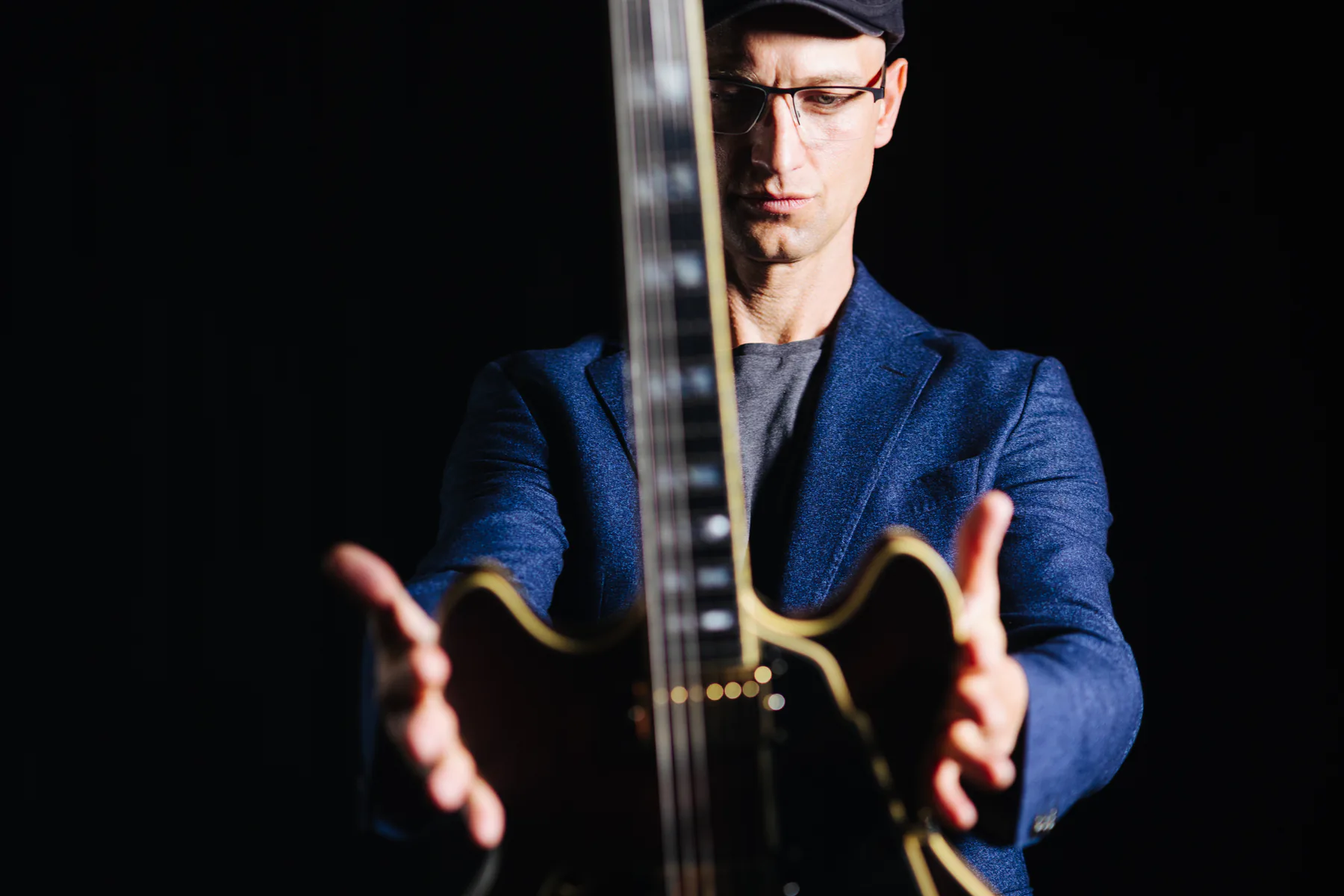 Pete Roth holding his guitar toward the camera in a dramatic colour portrait.