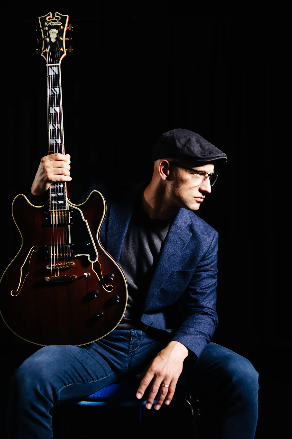 Pete Roth seated in profile with his red guitar in a colour portrait.